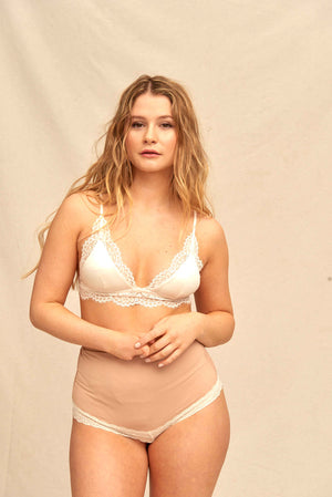 SIIL stomalingerie in creme met kant Blonde vrouw in crème kanten beha en Sofía stomalingerie in creme met hoge taille, handen op de buik